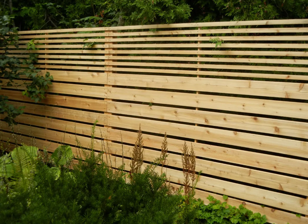 Horizontal wood privacy fence beside a green backyard lawn in the growing season.